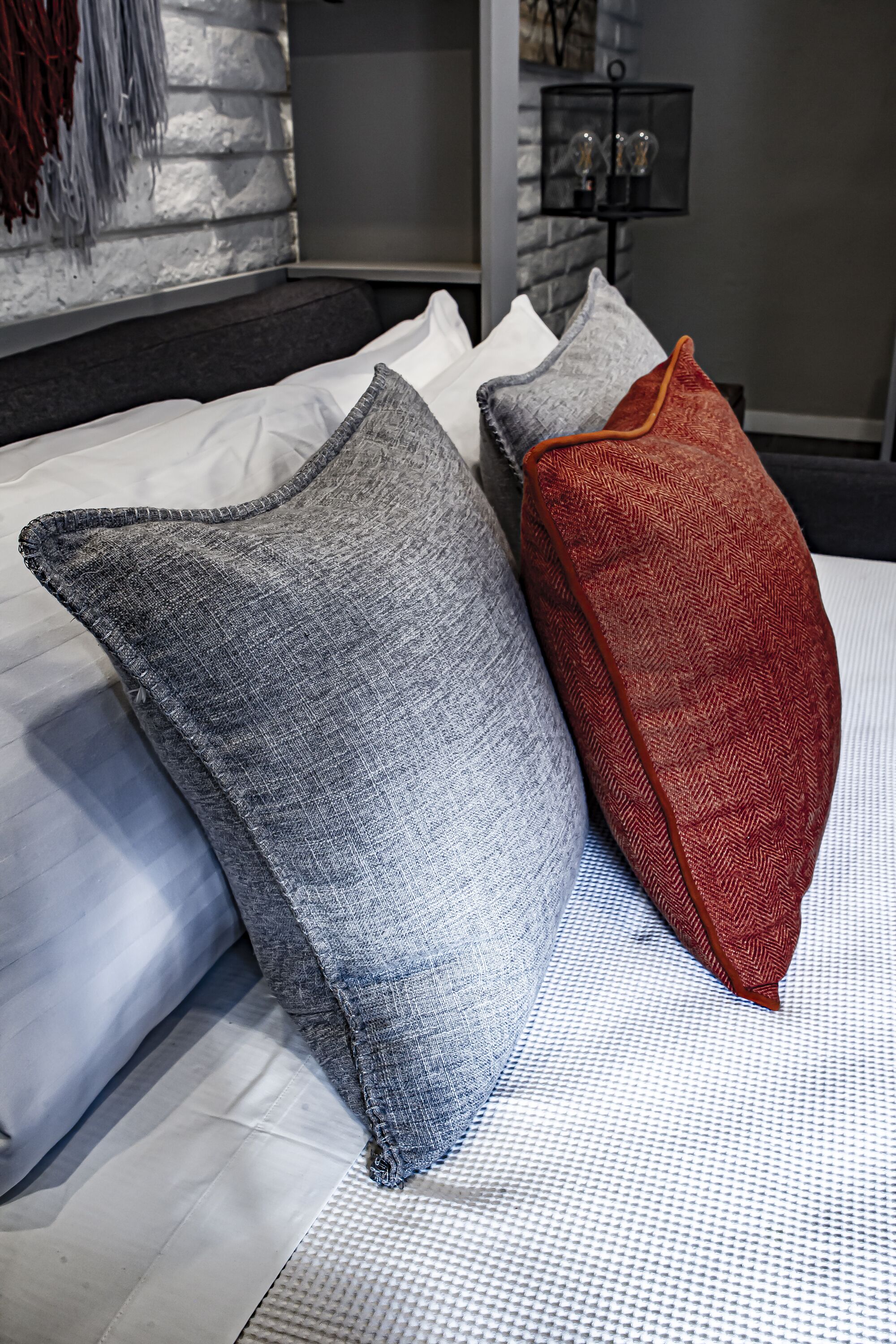 A bed with white and grey pillows and a red pillow.