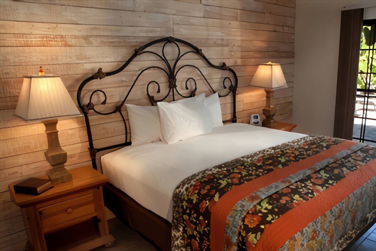 A neatly made bed with a floral bedspread, two bedside lamps, and a wooden nightstand with a book.