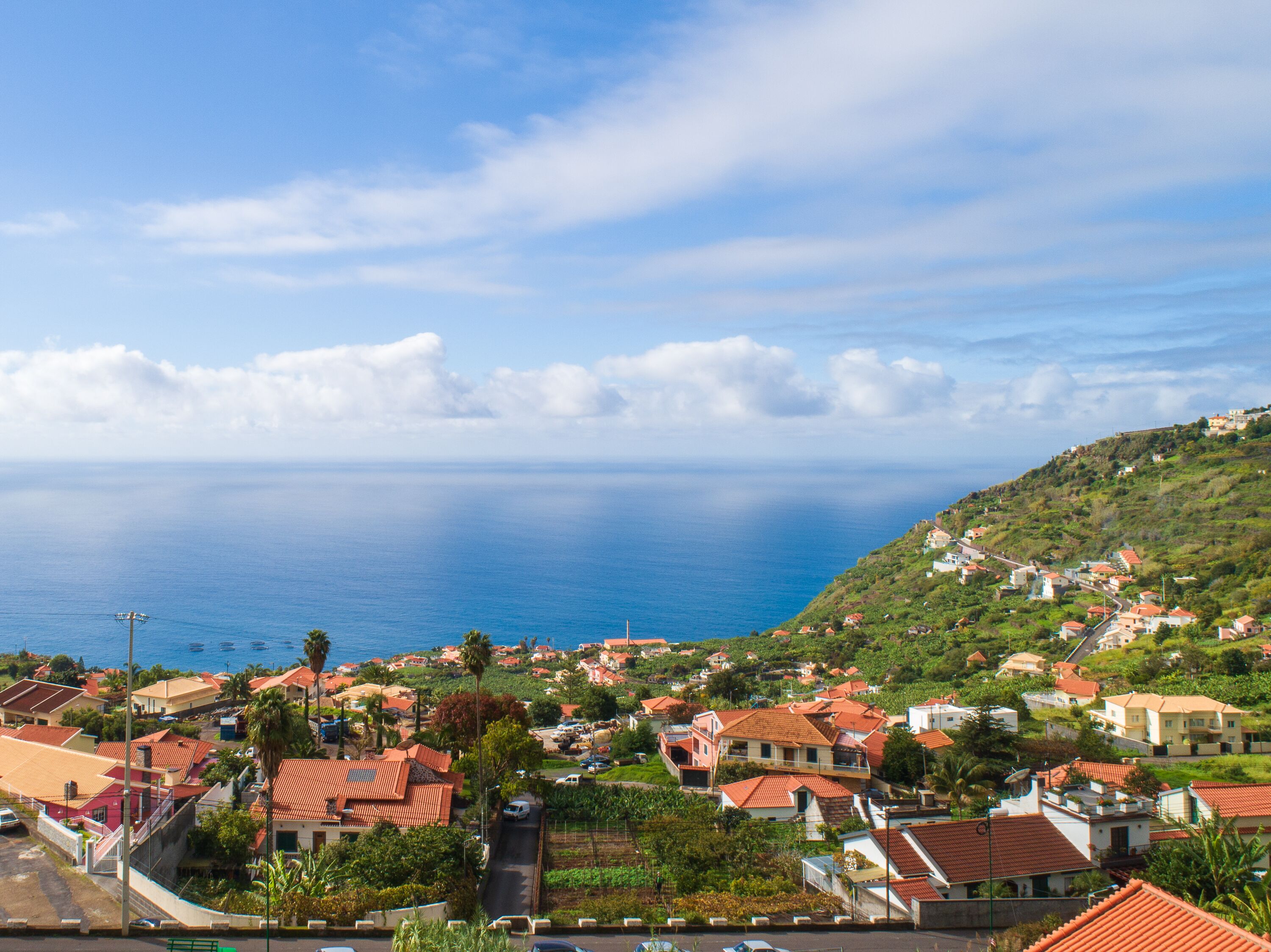Une ville côtière aux maisons aux toits rouges, offrant une vue dégagée sur la mer et s’étendant sur un paysage vallonné.