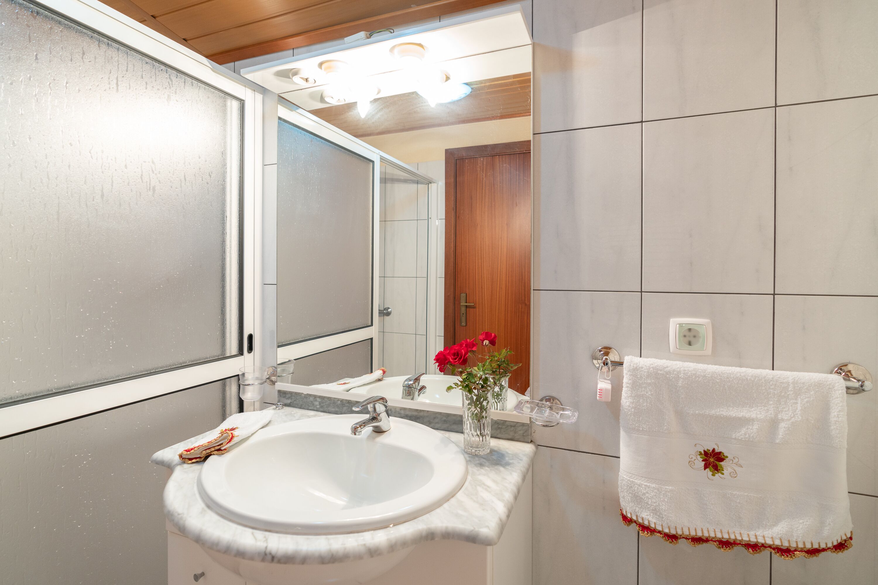 Une salle de bain avec un lavabo blanc, un miroir et une serviette à motifs floraux.