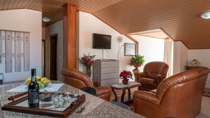 A cozy living room with leather chairs, a dining table with a bottle, glasses, and a bowl of fruit. There's a TV mounted on the wall and a potted plant on a small table. - Apartment Lucy , Sunning views over sea and mountains (Arco Da Calheta)