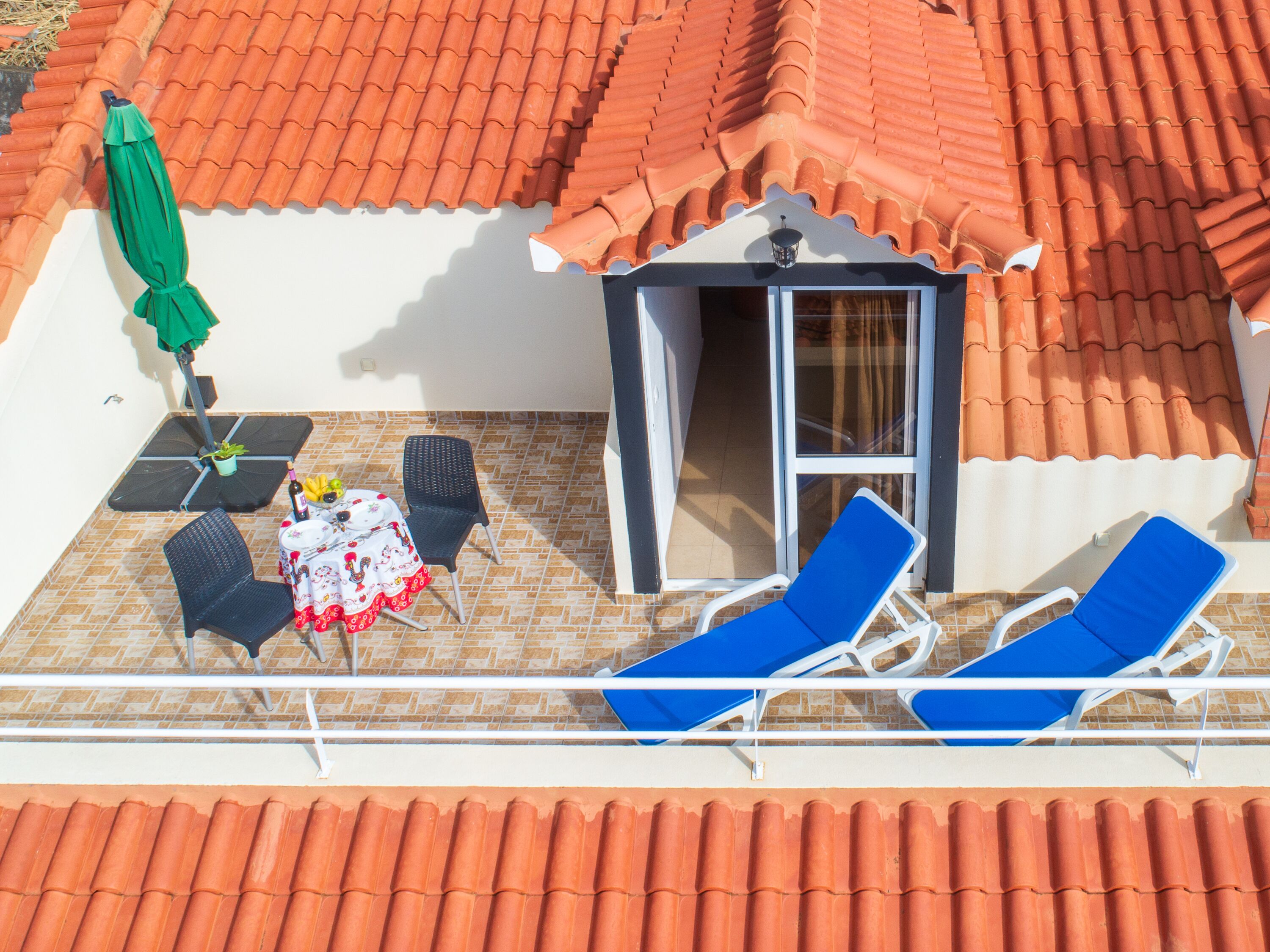 Une terrasse dotée d’un toit en tuiles, une table avec des chaises et deux transats.