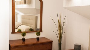 Une commode en bois avec un miroir au-dessus, une petite plante en pot et un grand vase contenant des roseaux.