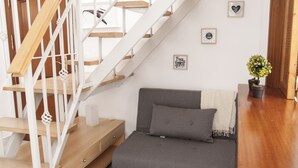 Un escalier avec des rampes blanches et des marches en bois, un canapé gris avec un coussin et une petite plante en pot posée sur le sol.
