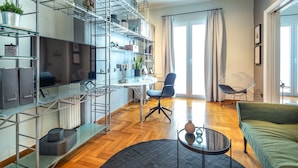A modern living room with a glass shelving unit, a green sofa, a round coffee table, and a dining area with a chair and table. - UPSTREET Superb 1BD Apt-Heart of Kolonaki (Athens)