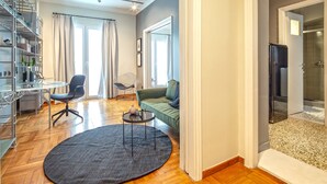 A modern living room with a round rug, a green sofa, a glass coffee table, and a metal shelving unit. - UPSTREET Superb 1BD Apt-Heart of Kolonaki (Athens)