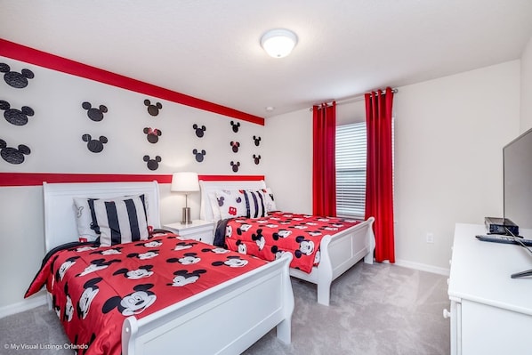 A bedroom with two beds, red curtains, and Mickey Mouse wall decals.