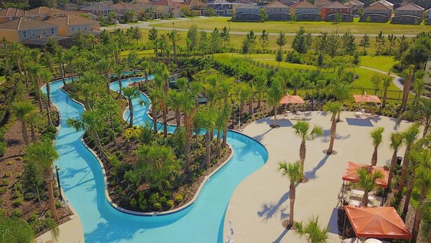 A resort with a winding pool, palm trees, and a view of nearby houses. - Stylish and Stunning 5BD Pool Home in Solterra - #5st452 (Davenport)