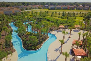 A resort with a winding pool, palm trees, and a view of nearby houses.