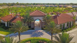 A residential area with houses featuring red-tiled roofs and stucco walls, surrounded by lush greenery and palm trees. - Stylish and Stunning 5BD Pool Home in Solterra - #5st452 (Davenport)