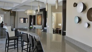 A modern kitchen with a curved island, bar stools, pendant lighting, and a large painting on the wall. - Stylish and Stunning 5BD Pool Home in Solterra - #5st452 (Davenport)