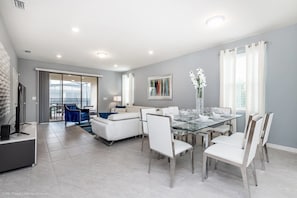 A modern living room with a glass dining table, white sofas, and a view to the outside.