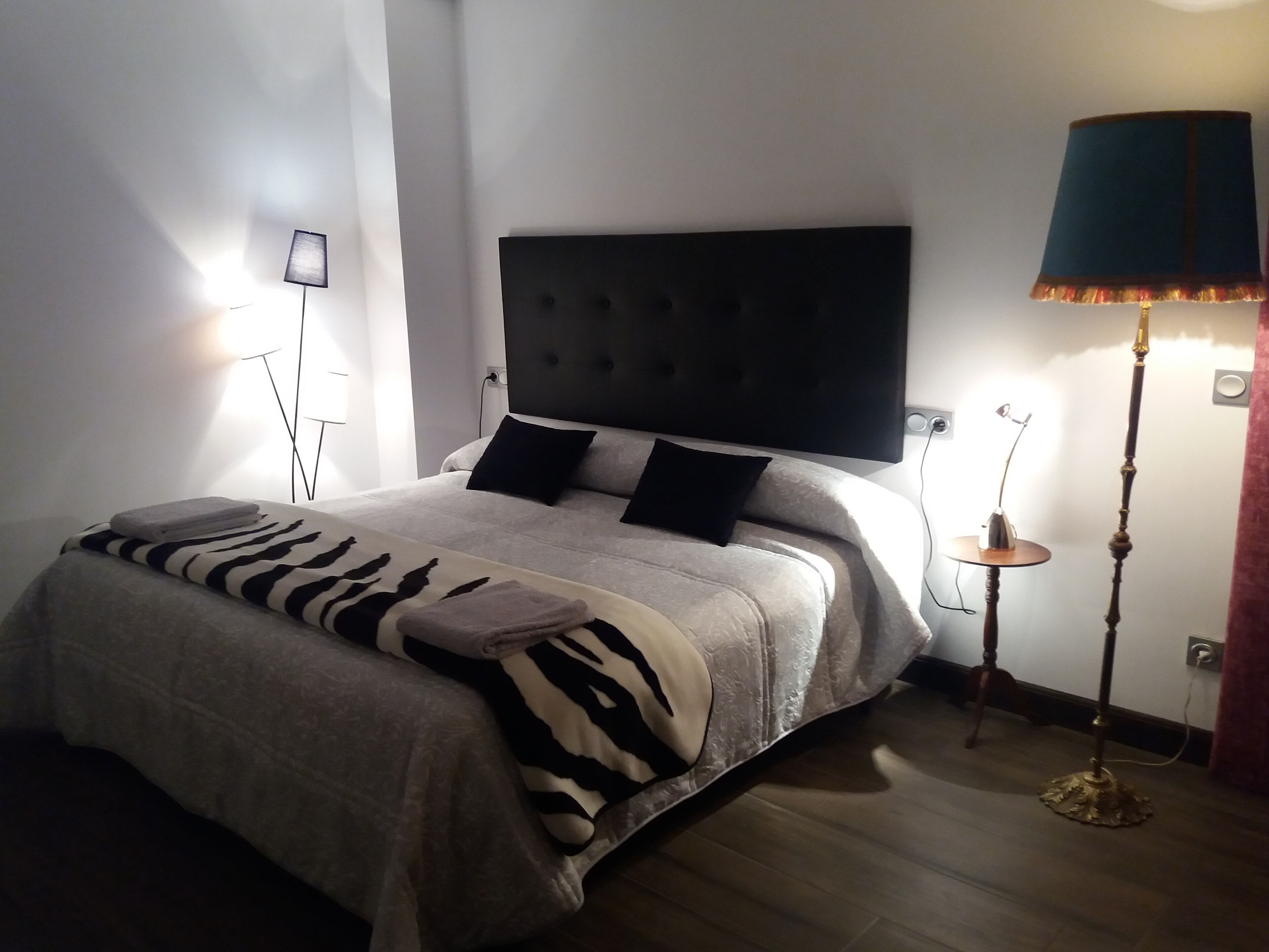 A neatly made bed with a zebra-patterned blanket, a dark headboard, and two black pillows.