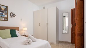 Hotellihuone, jossa on sänky, vaatekaappi, yöpöytä lampun kanssa ja ovi.