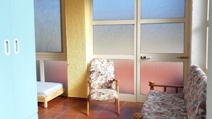 A room with a bed, two chairs, a wardrobe, and large windows with screens.