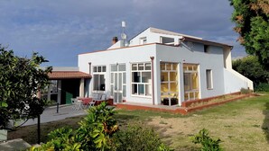A modern two-story house with a flat roof, large windows, and a small patio area with outdoor furniture.