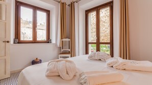 Ett hotellrum med två sängar, utsikt över en byggnad i sten och ett fönster med gardiner.