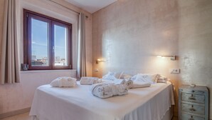 Een hotelkamer met een groot bed, een raam met gordijnen, een wandlamp en een klein houten dressoir.