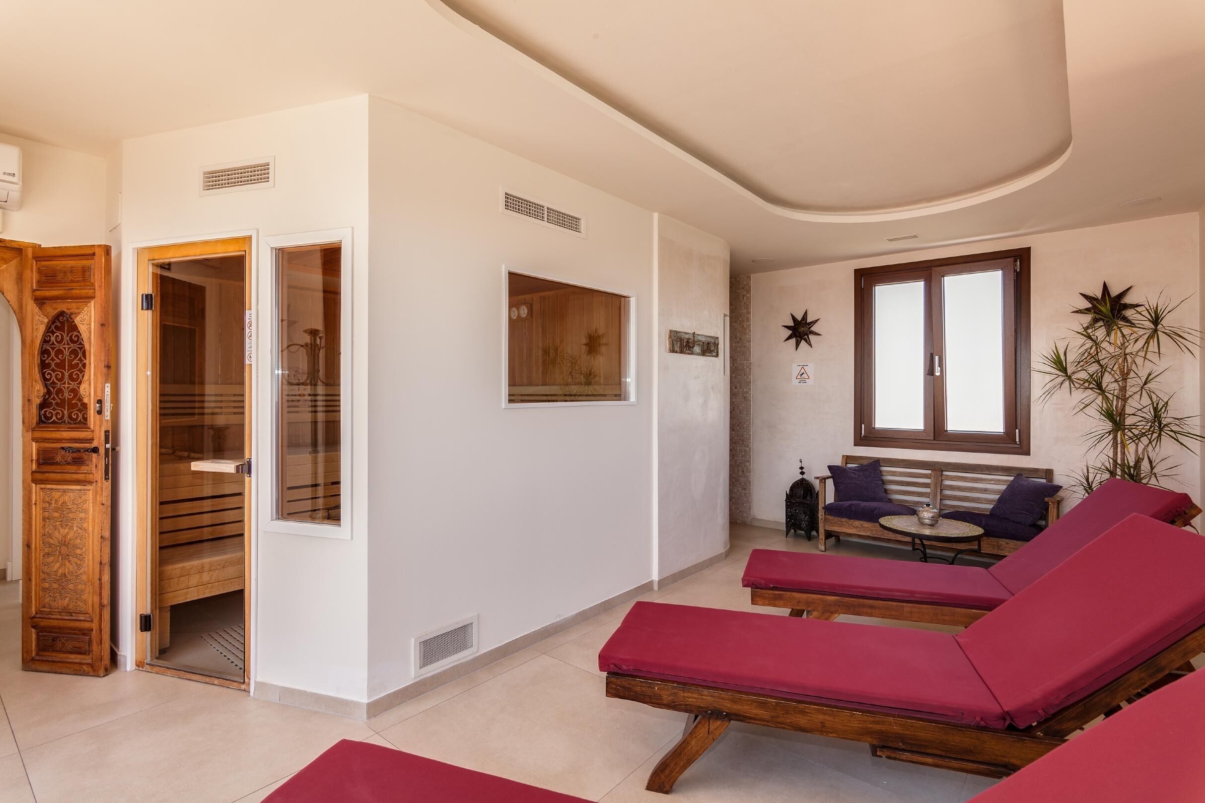 A spa room with wooden benches, a bench with a table, and a window with blinds.