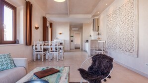 Een ruime woonkamer met een eettafel en stoelen, een bank, een decoratieve wand en een groot raam.