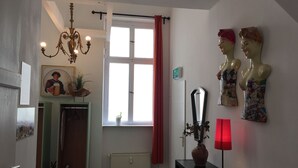 Une pièce avec un lustre, une fenêtre ornée de rideaux rouges, un miroir et deux bustes décoratifs accrochés au mur.