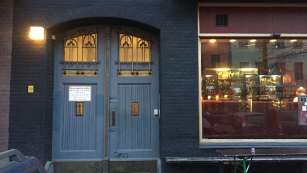 Un bâtiment à la façade sombre, une grande fenêtre reflétant les lumières et une enseigne sur la porte.