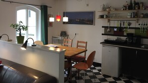 Une cuisine compacte avec un coin repas, dotée d’un sol à carreaux, de poutres en bois, d’une plante en pot et offrant une vue sur le paysage urbain.