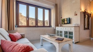 A living room with a sofa, a coffee table, a cabinet, and a large window with a view of a rocky landscape. - Apartment porch and garden (Tarifa)