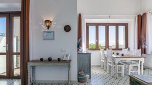 A dining area with a table and chairs, a wall-mounted light fixture, and a window with curtains. - Apartment porch and garden (Tarifa)