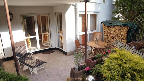 A covered patio with a seating area, a fire pit, and a stack of firewood. - Idyllic and quietly located vacation apartment in the university town of Idstein🌳 (Idstein)