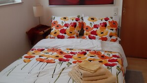 A neatly made bed with a floral bedspread, a large painting of a rose on the wall, and a bedside table with a lamp. - Idyllic and quietly located vacation apartment in the university town of Idstein🌳 (Idstein)