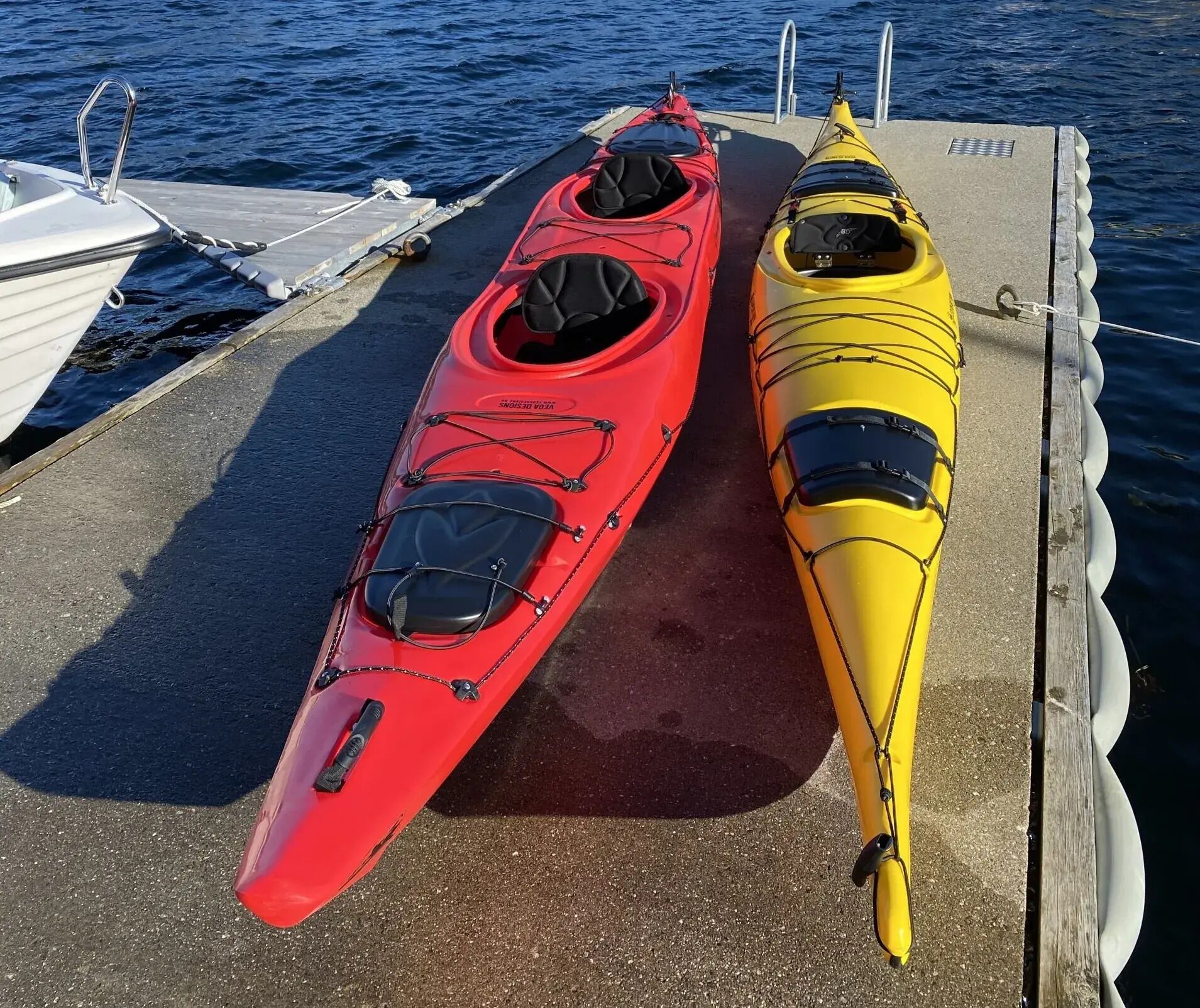 Zwei Kajaks, ein rotes und ein gelbes, liegen an einem Steg, im Hintergrund ein Boot.