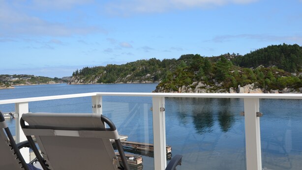 A deck with a glass railing overlooking a calm body of water and a forested island. - Fishing, 2 top boats, swimming, SUP, workation, relaxing, everything is possible (Urangsvåg)