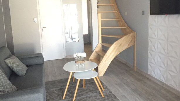 A modern living room with a grey sofa, a small round table with a vase, and a wooden spiral staircase.