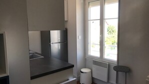 Eine kleine Küche mit integriertem Kühlschrank, einem kleinen Mülleimer und einem Fenster für natürliches Licht.