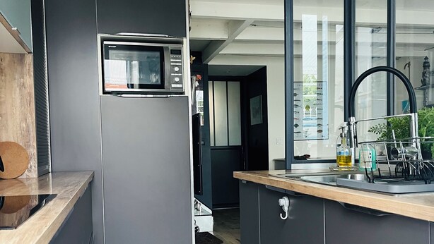 Une cuisine moderne avec des meubles de couleur grise, un four à micro-ondes encastré et un plan de travail en bois.