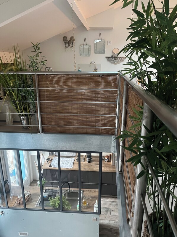 A modern interior with a bamboo partition, a kitchen area with a coffee machine, and a view of the dining area through a glass railing.