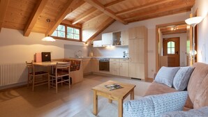 A cozy, well-lit room with a wooden ceiling, a dining table with chairs, a sofa, and a kitchen area with cabinets and a stove.