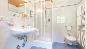 A bathroom with a glass-enclosed shower, a white sink, and a bidet.
