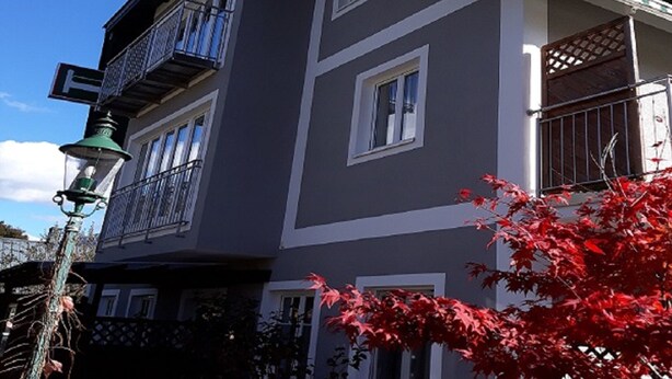 Un immeuble à plusieurs étages doté d’un balcon, d’un lampadaire et d’un arbre aux feuilles rouges.