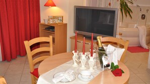 Un coin repas avec une table dressée pour deux personnes, un téléviseur et, au fond, une baignoire.