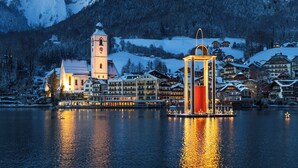 Une ville au bord d’un lac, avec un clocher d’église imposant, un château d’eau illuminé et des bâtiments recouverts de neige.