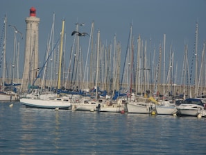 A marina with numerous boats docked, a lighthouse in the background, and a clear sky.