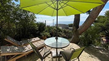 Une terrasse avec une table et des chaises, un parasol jaune et une vue sur la mer.