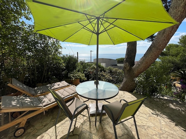 A patio with a table and chairs, a yellow umbrella, and a view of the sea.
