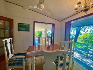 Enjoy meals in this dining area with a table, chairs, and a chandelier, surrounded by a view of lush greenery.