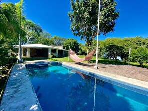 Relax by the serene pool surrounded by lush greenery and palm trees, perfect for a leisurely day.