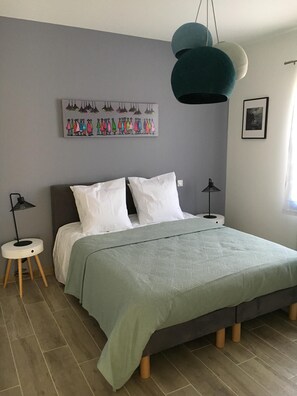 A bedroom with a bed, two bedside tables, a floor lamp, a wall art piece, and a framed picture.