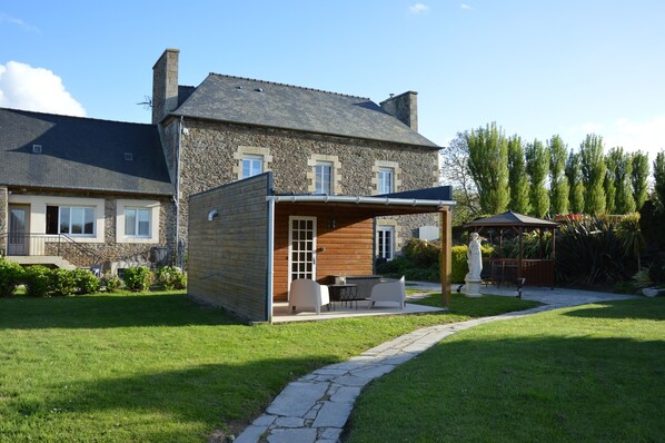 A stone house with a wooden extension, a stone pathway, and a gazebo.