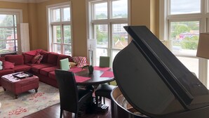 A living room with a red sofa, a dining table with chairs, and a grand piano.